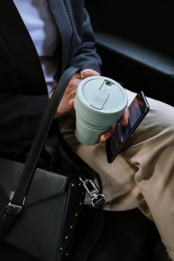 Services-03 Person holding reusable coffee cup and smartphone in a car, depicting eco-friendly commute.